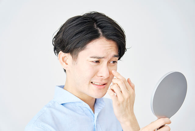 手鏡で目を見る男性